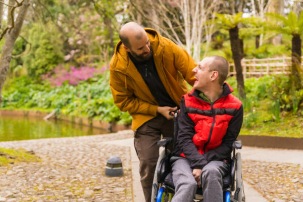 a person with a disability in the wheelchair being pushed by a friend in a public city park, having fun in spring