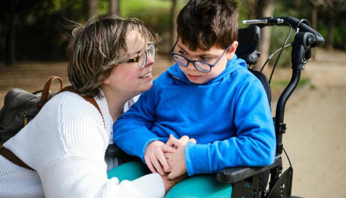 Disabled boy in a wheelchair enjoying a walk outdoors with his mother.